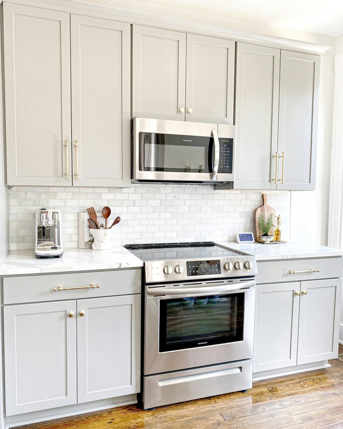 Modern kitchen with silver appliances, light gray cabinets, and a tiled backsplash.
